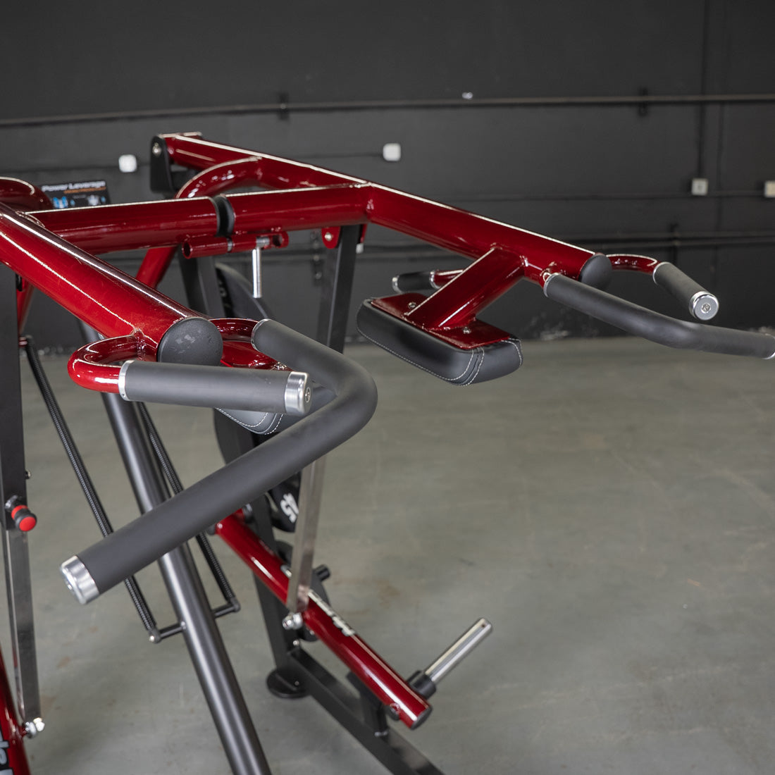 Close-up of a red Viking press machine with black padded handles and arm rests.
