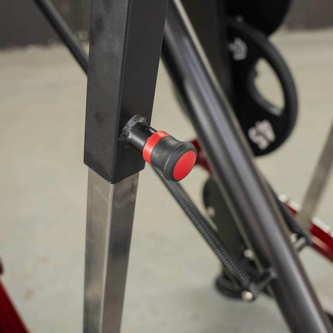 Close-up of a black and red adjustment knob on a fitness machine, with a 45lb weight plate in the background.