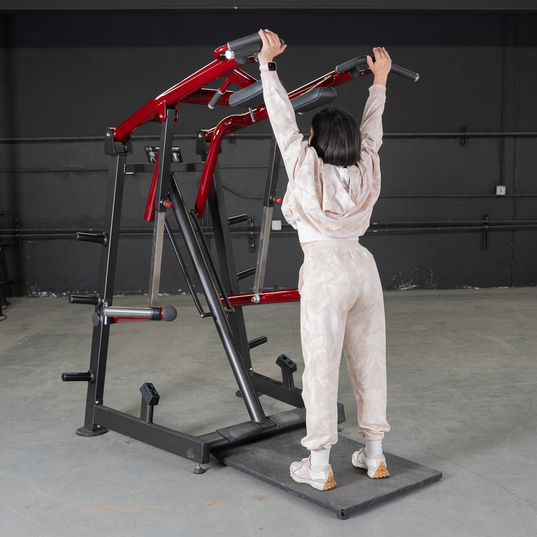 Woman using a red and black Viking press machine, standing on a platform with hands on the handles.
