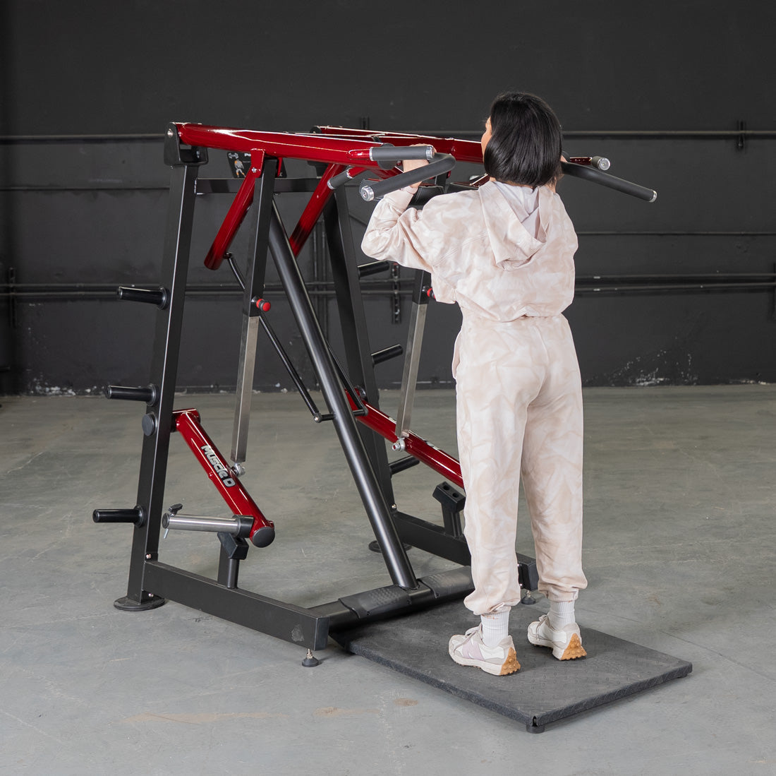 Woman using a red and black Viking press machine for a shoulder workout.