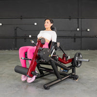 Thumbnail for Woman in pink leggings using a red and black leg extension/curl machine with a 25lb weight plate.