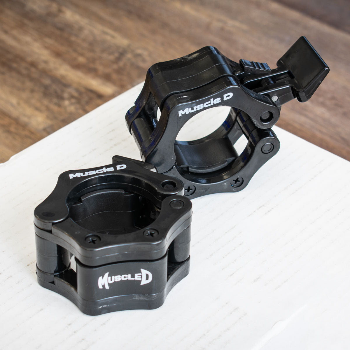Pair of black Muscle D Fitness Olympic bar collars, one open and one closed.