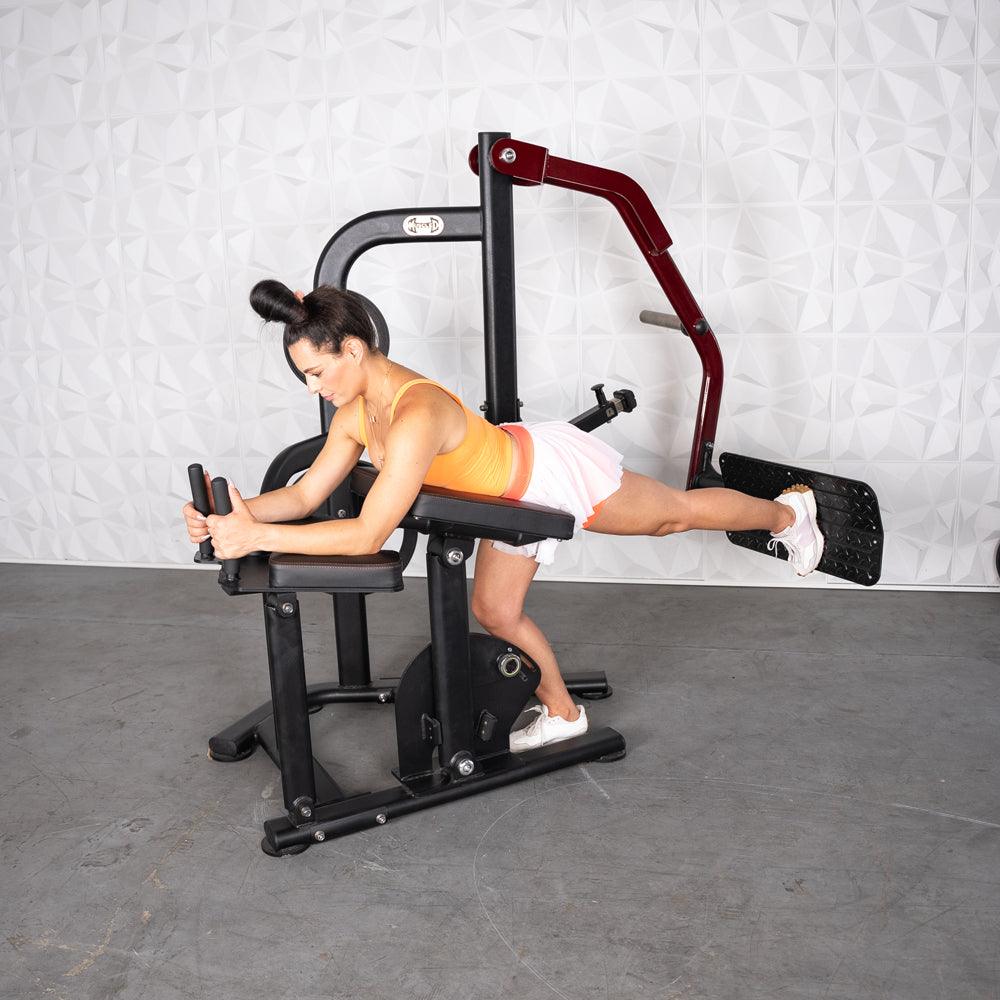 Woman using a black and red glute kickback machine, extending her right leg backward.