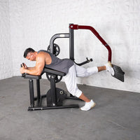 Thumbnail for Man using a black and red plate-loaded glute kickback machine, lying prone with one leg extended.