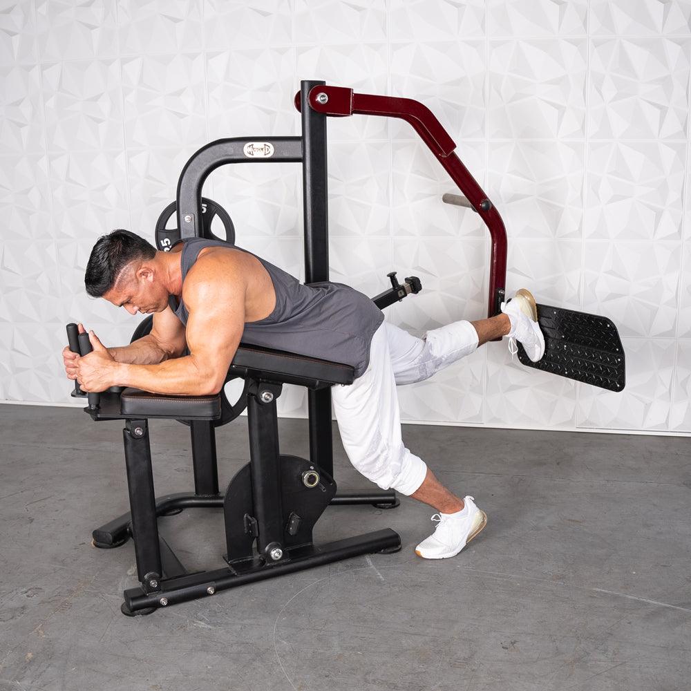 Man using a black and red glute kickback machine, pushing a footplate with his right leg.