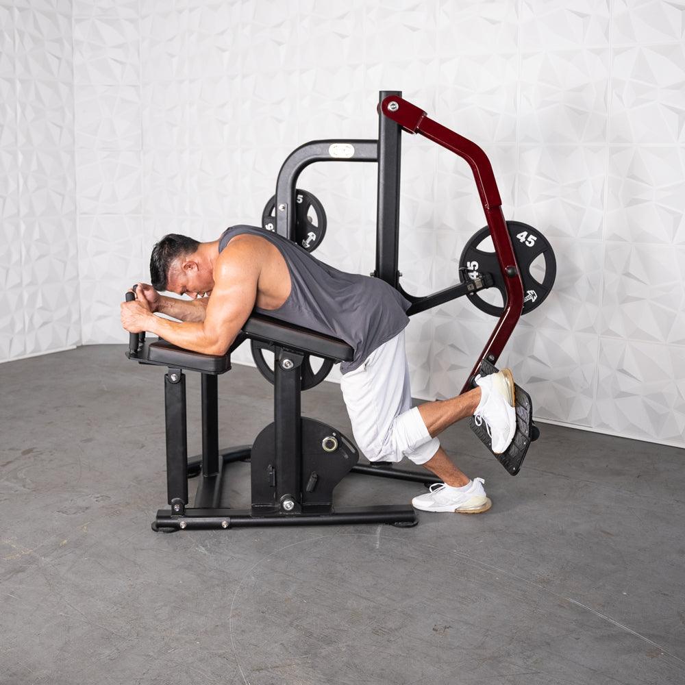 Man using a plate-loaded glute kickback machine, lying face down on the pad, pushing with his leg.