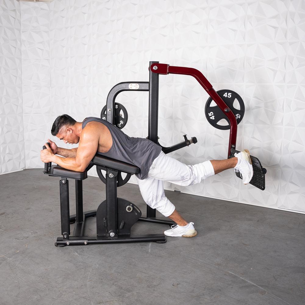 Man using a plate-loaded glute kickback machine, lying prone on the bench and extending his leg.