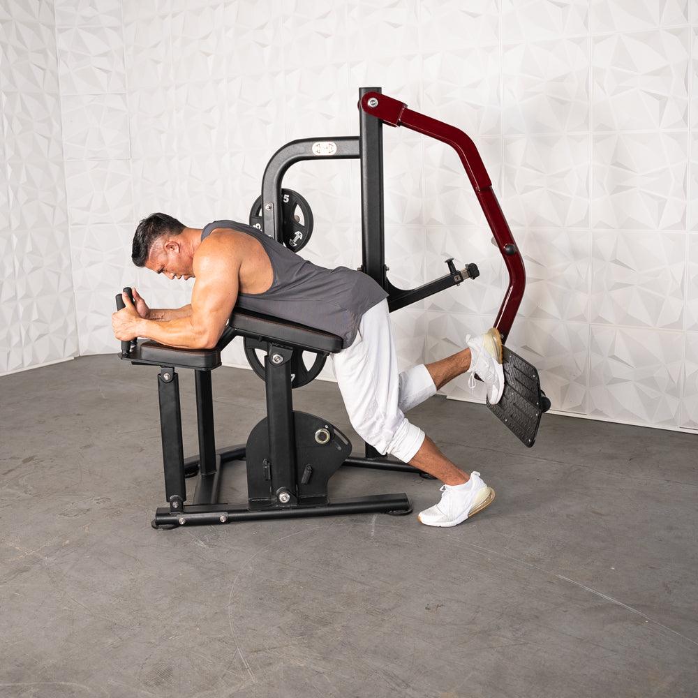 Man using a black and red glute kick machine, lying prone on the pad and pushing the footplate.