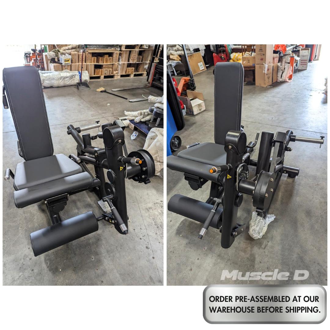 Black plate-loaded leg extension/curl machine with padded seat and backrest, shown from two angles in a warehouse.