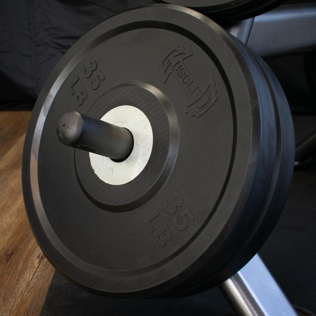 Black 35 lb bumper plate with "MUSCLE D" logo on a weight rack.
