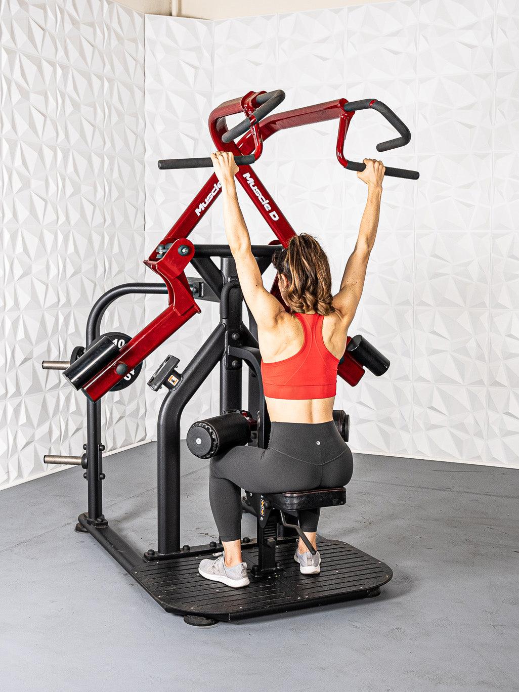 Woman using a red and black rotary lat pull-down machine, gripping the handles overhead.