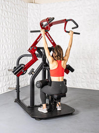Thumbnail for Woman using a red and black rotary lat pull-down machine, gripping the handles overhead.