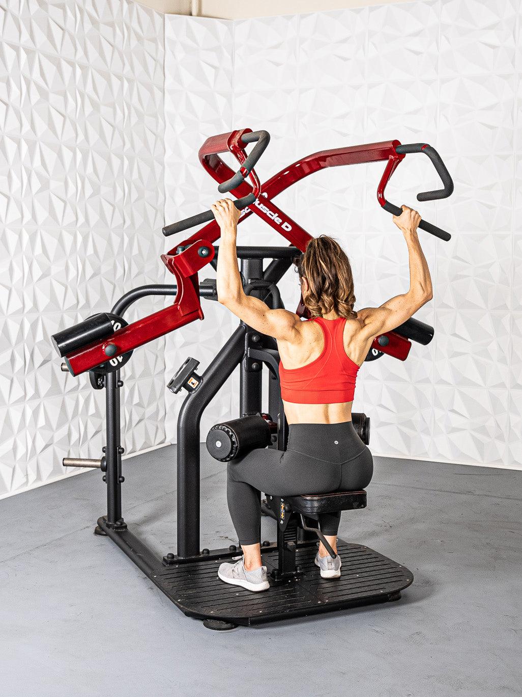 Woman in red top and black leggings using a red and black rotary lat pull-down machine.