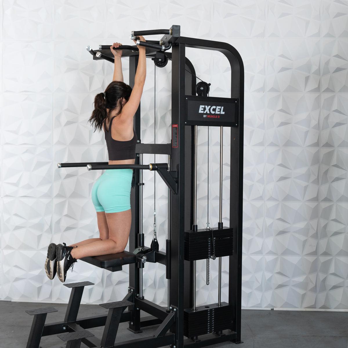 Woman using a black assisted chin/dip machine with adjustable handles and knee pad.