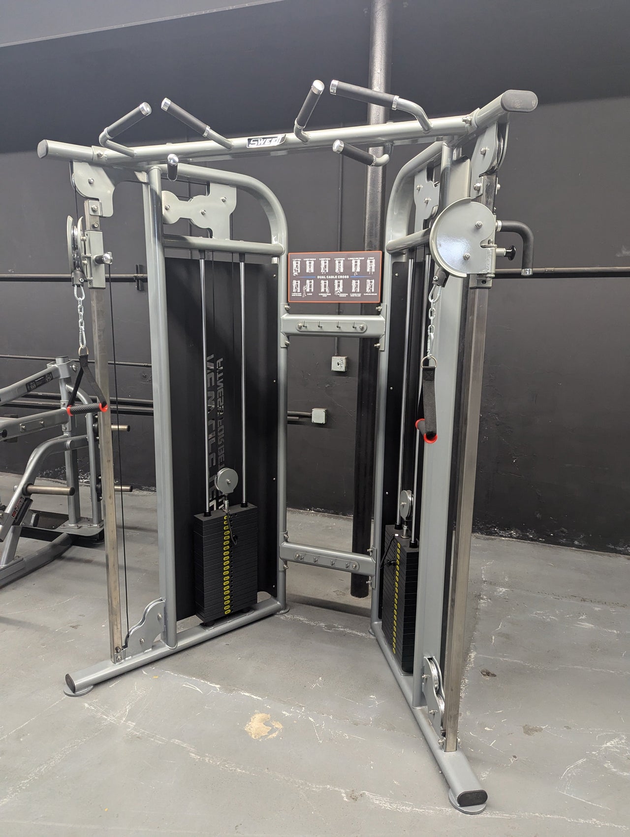 Dual adjustable pulley cable machine with weight stacks and pull-up bar in a gym setting.