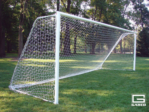 White soccer goal with a net on a green grassy field with trees in the background.