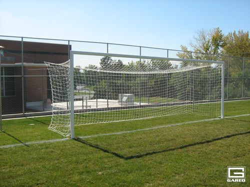 White soccer goal with net on a green grass field under a clear blue sky.