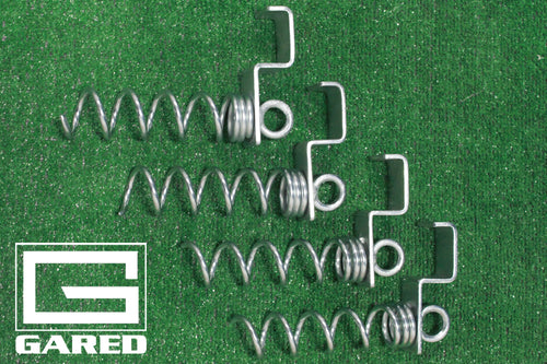 Four metal screw anchors with springs and hooks on green turf.