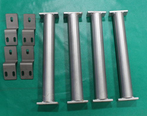 Four metal tube anchors with flat bases and eight L-shaped brackets with slotted holes on a green surface.
