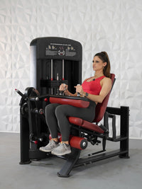 Thumbnail for Woman in red top and gray leggings using a black and red leg extension/curl combo machine.