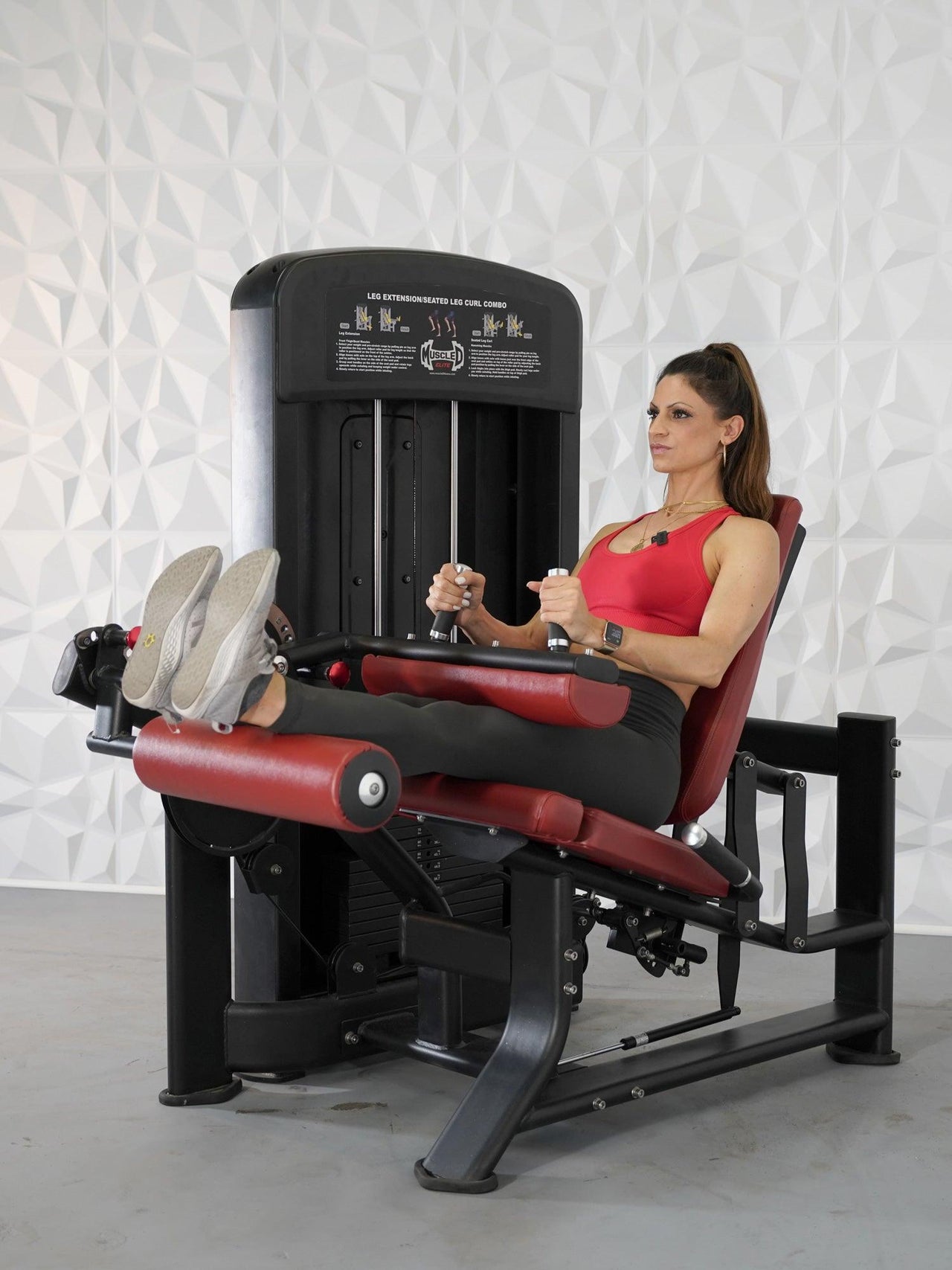 Woman in red top and black leggings using a black and red leg extension/curl combo machine.