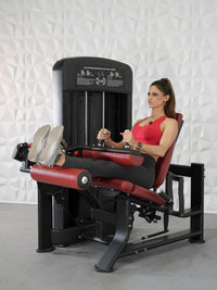 Thumbnail for Woman in red top and black leggings using a black and red leg extension/curl combo machine.