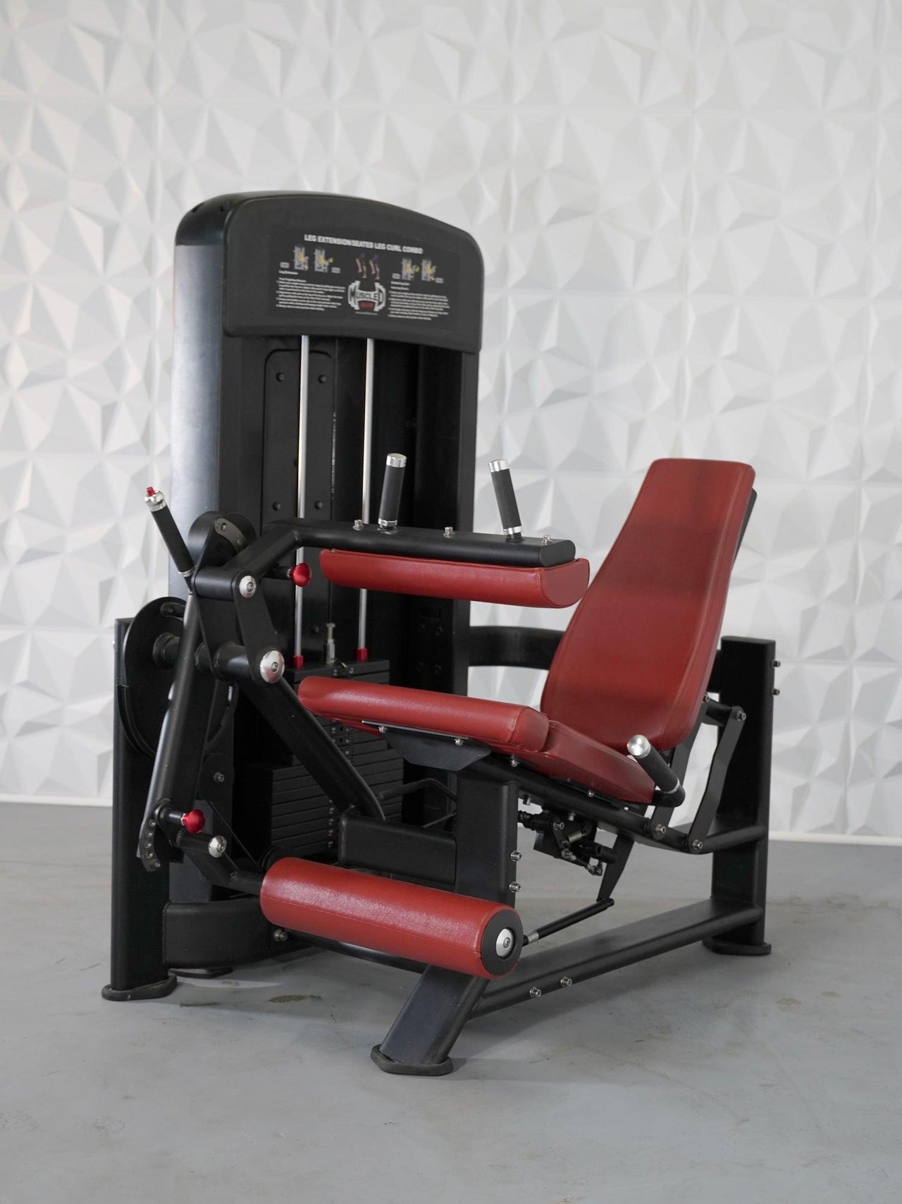 Black and red leg extension and seated leg curl combo machine with a weight stack.