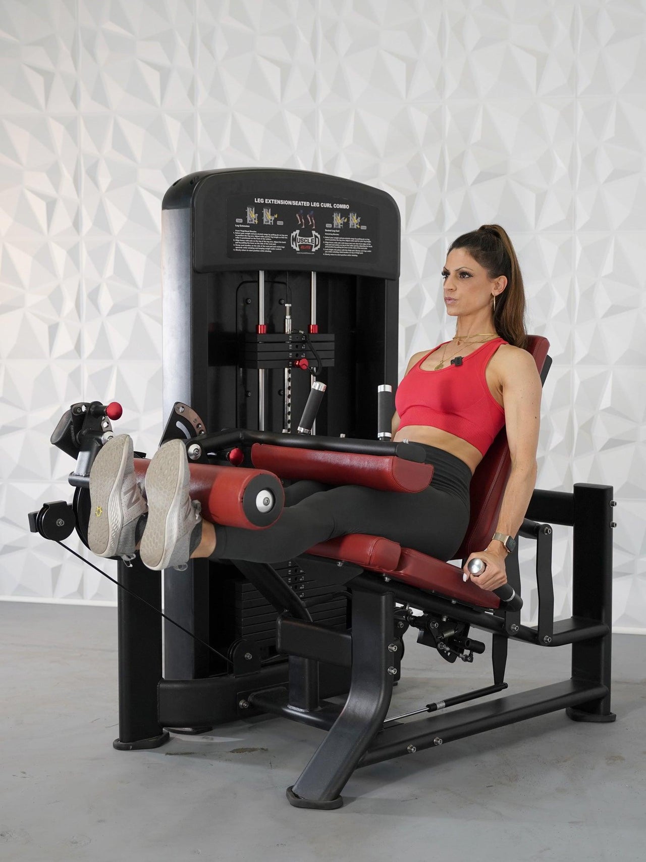Woman in red top using a black and red leg extension and curl machine.
