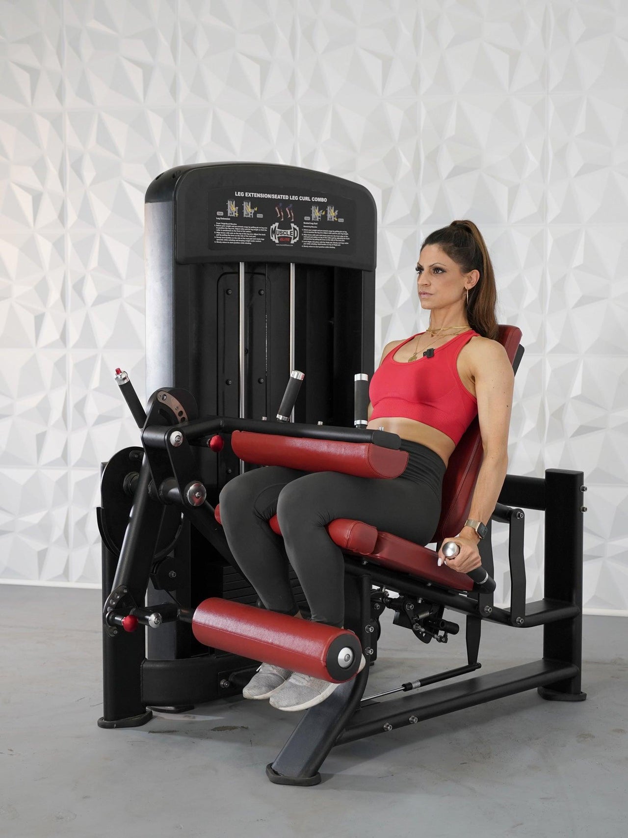 Woman in red top using a black and red leg extension and seated leg curl combo machine.