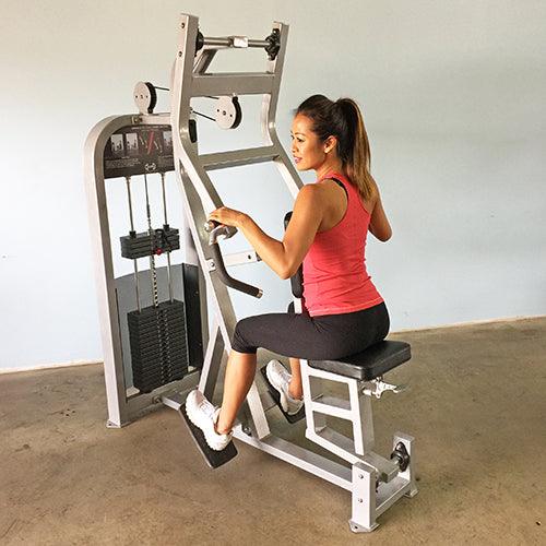 Woman in red tank top and black capris using a silver seated row machine with pin selectorized weights.
