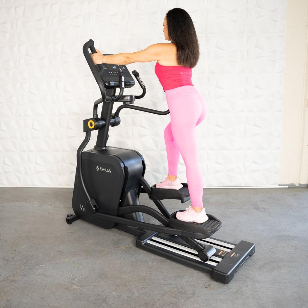 Woman in pink activewear exercising on a black commercial cross trainer elliptical.
