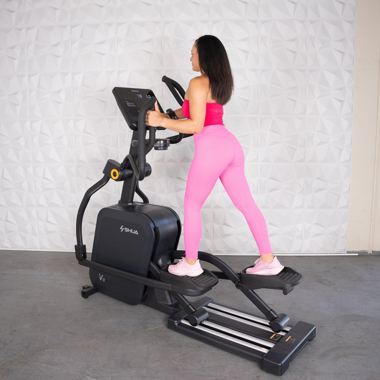 Woman in pink activewear using a black commercial elliptical machine.