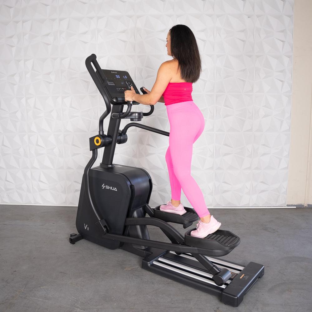 Woman in pink exercising on a black commercial cross trainer elliptical.