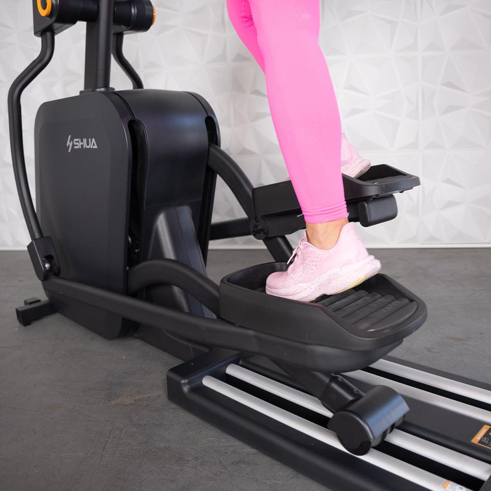 Person in pink leggings and sneakers using a black elliptical machine.