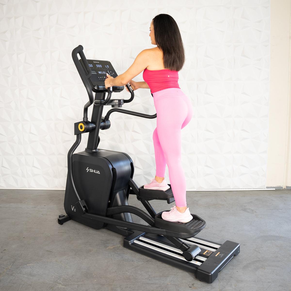 Woman in pink activewear using a black commercial elliptical cross trainer.