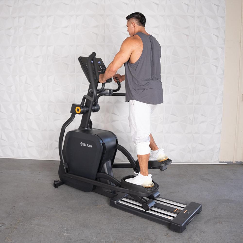 Man in gray tank top and white shorts using a black elliptical cross trainer.