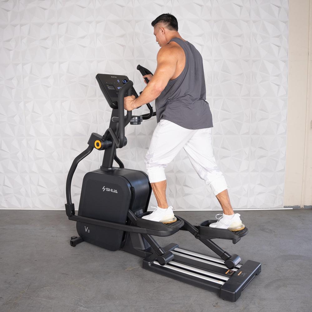 Man in tank top and white pants exercising on a black commercial cross trainer elliptical.