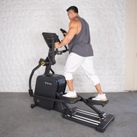 Thumbnail for Man in tank top and white pants exercising on a black commercial cross trainer elliptical.