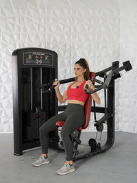 Thumbnail for Woman in red top and gray leggings using a black and red shoulder press machine.