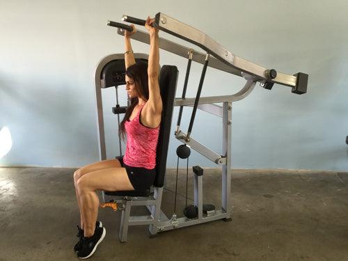 Woman using a shoulder press machine with an adjustable seat and pin selectorized weight stack.