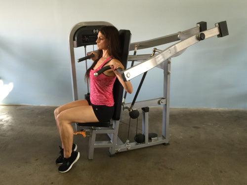 Woman in pink top and black shorts using a shoulder press machine.