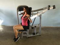 Thumbnail for Woman in pink top and black shorts using a shoulder press machine.