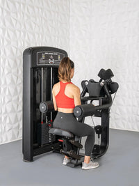 Thumbnail for Woman in red top and black leggings using a black side lateral raise machine.