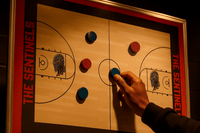 Thumbnail for Hand moving a blue magnet on a basketball court whiteboard with red and blue magnets, 