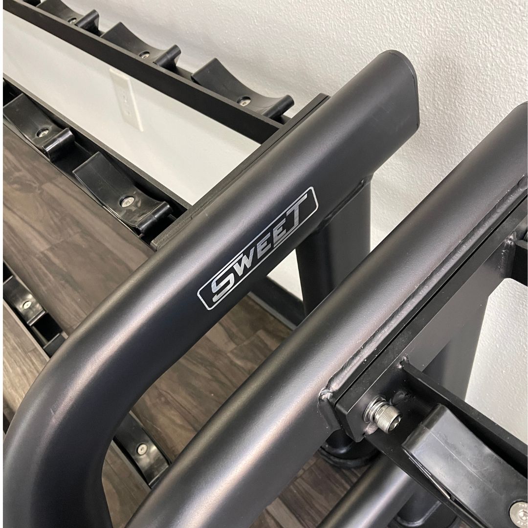 Close-up of a black "SWEET" branded 2-tier dumbbell rack with wood-grain shelves.