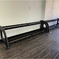 Thumbnail for Two empty black 2-tier dumbbell racks on a dark wood floor against a white wall.