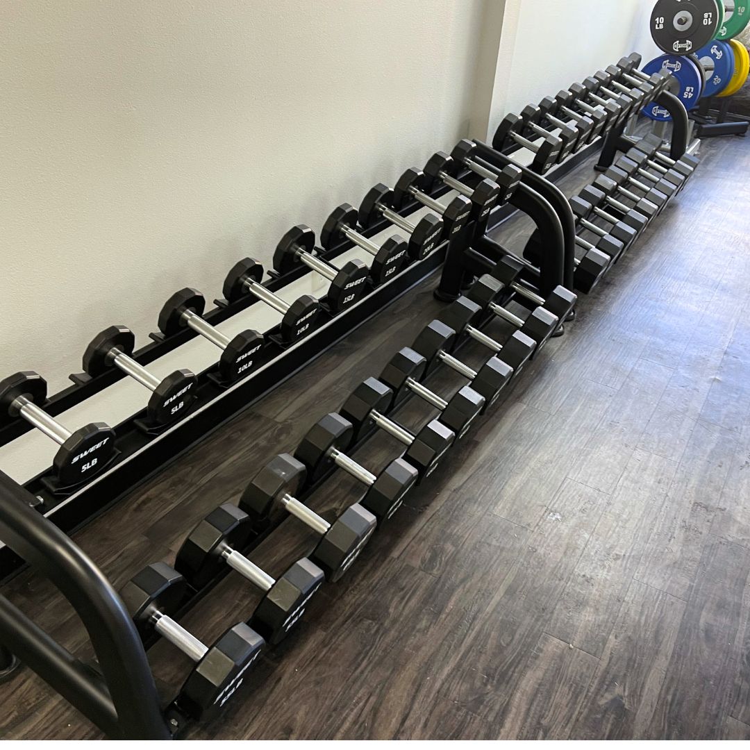 Two rows of black hexagonal dumbbells with silver handles on black racks.