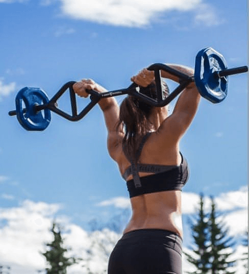 Woman lifting a black multi-grip bar with blue weight plates overhead against a blue sky.