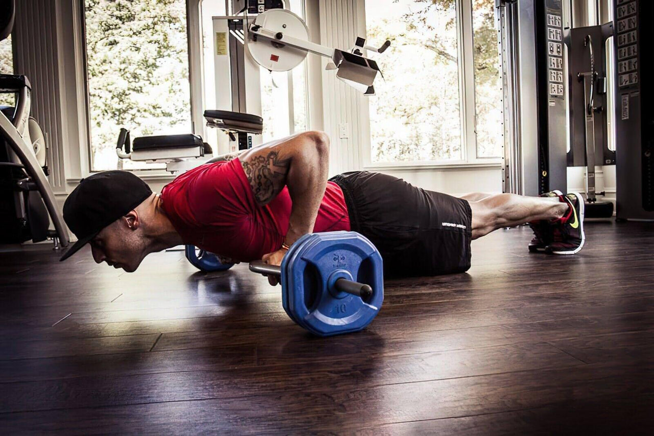 Man in red shirt and black shorts doing push-ups with a black TGrip Club Strength Bar with blue weights.