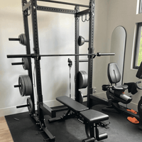 Thumbnail for Black half rack with barbell, weight plates, and adjustable bench in a home gym.